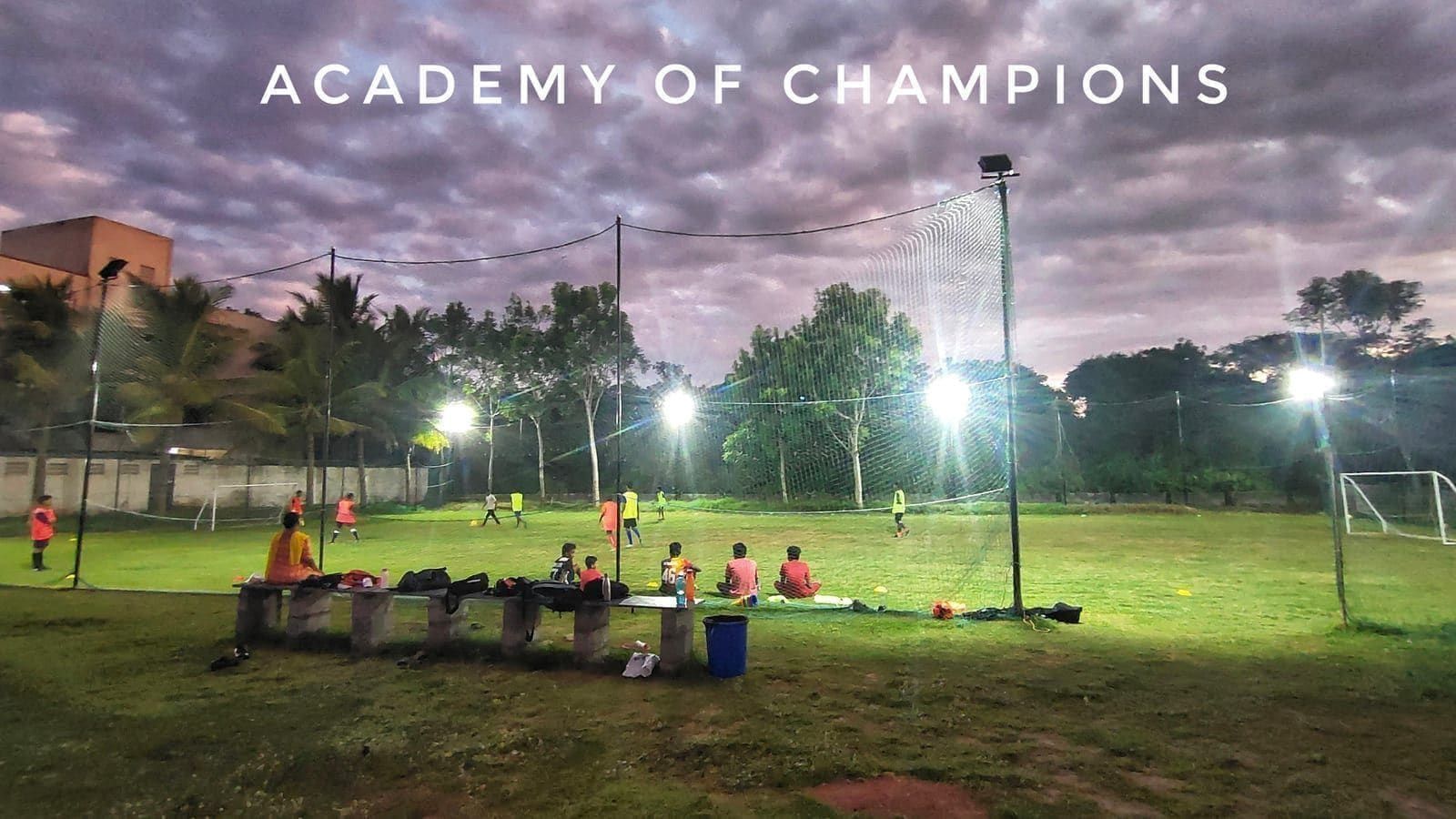 Players gathering on a floodlit field beneath a cloudy evening sky