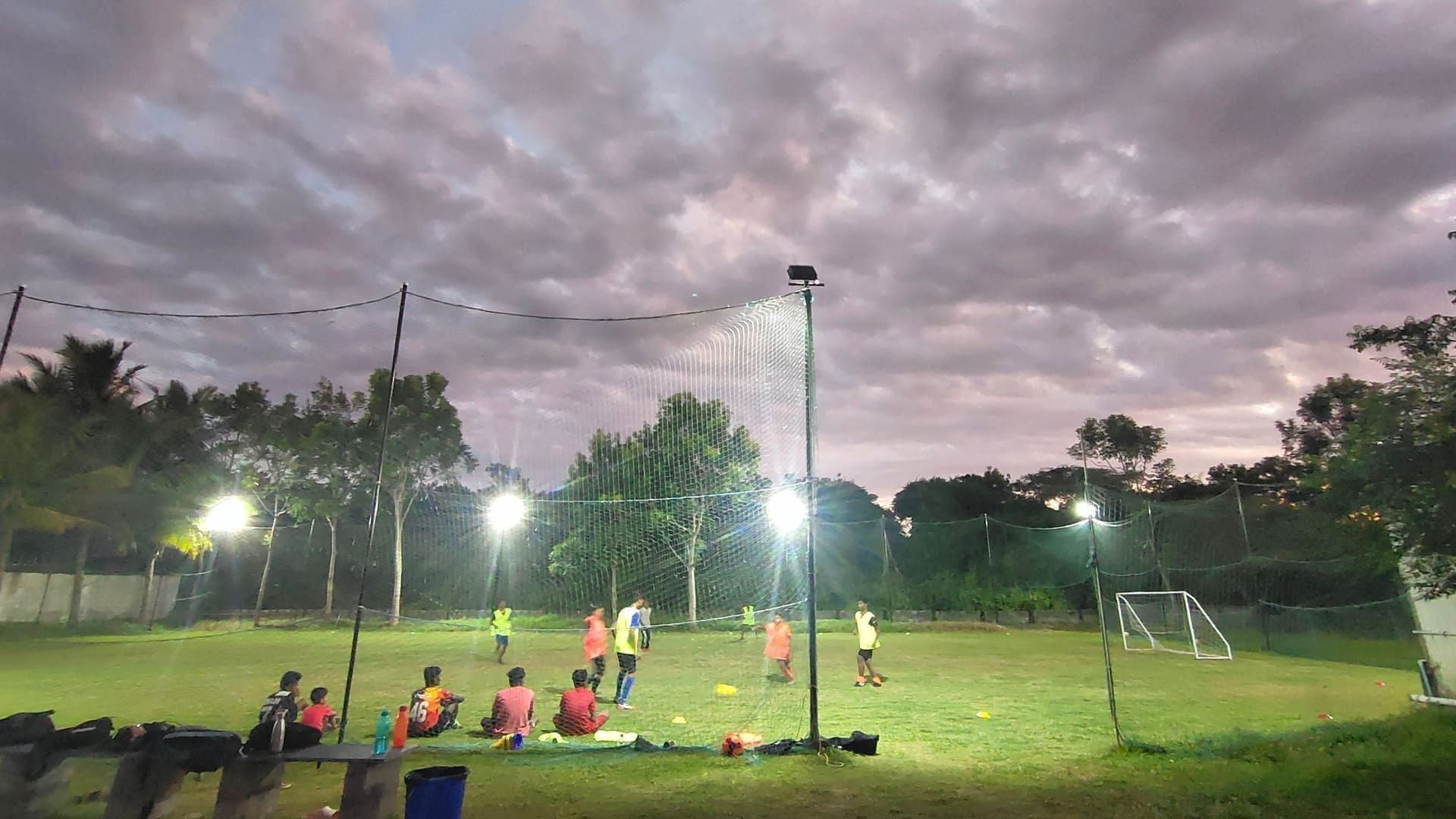 Young players training on a grass field as the floodlights come on