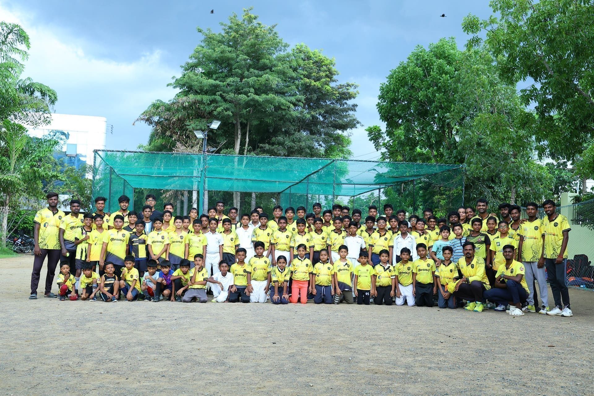 Young players and coaches posing in front of outdoor cricket nets