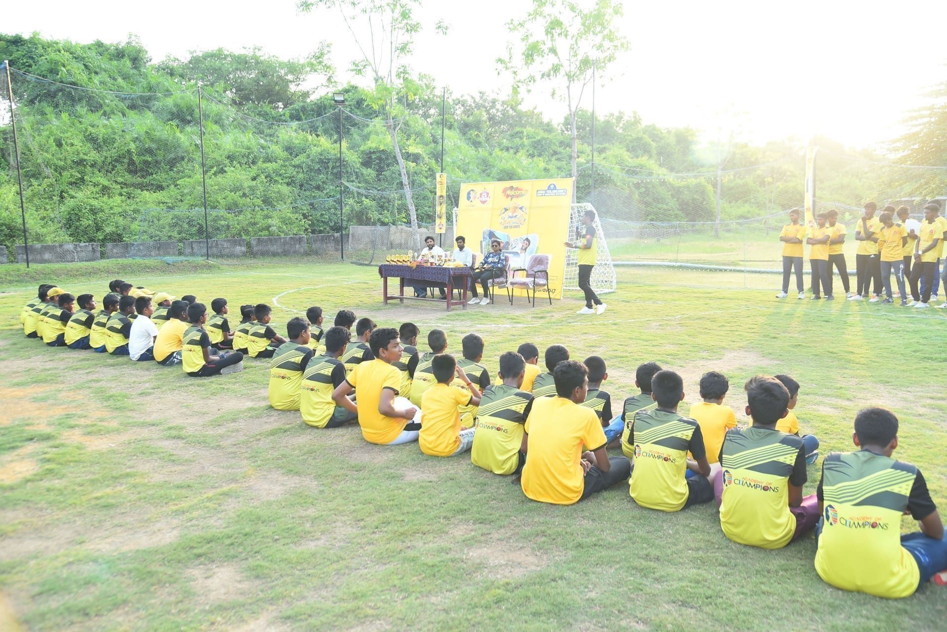 Young players seated on the grass facing a trophy presentation table