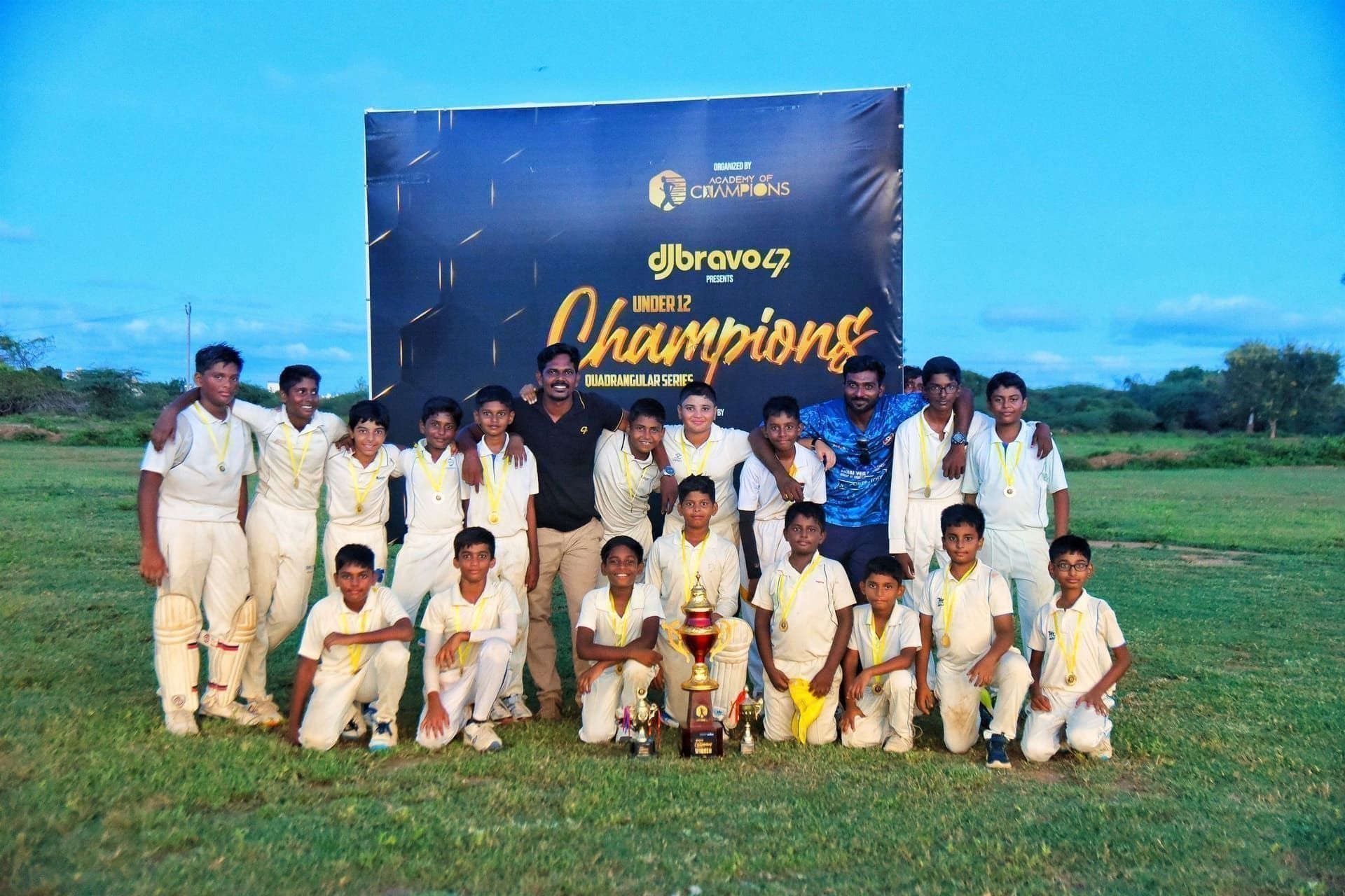 Junior cricket team posing with a trophy in front of a champions banner
