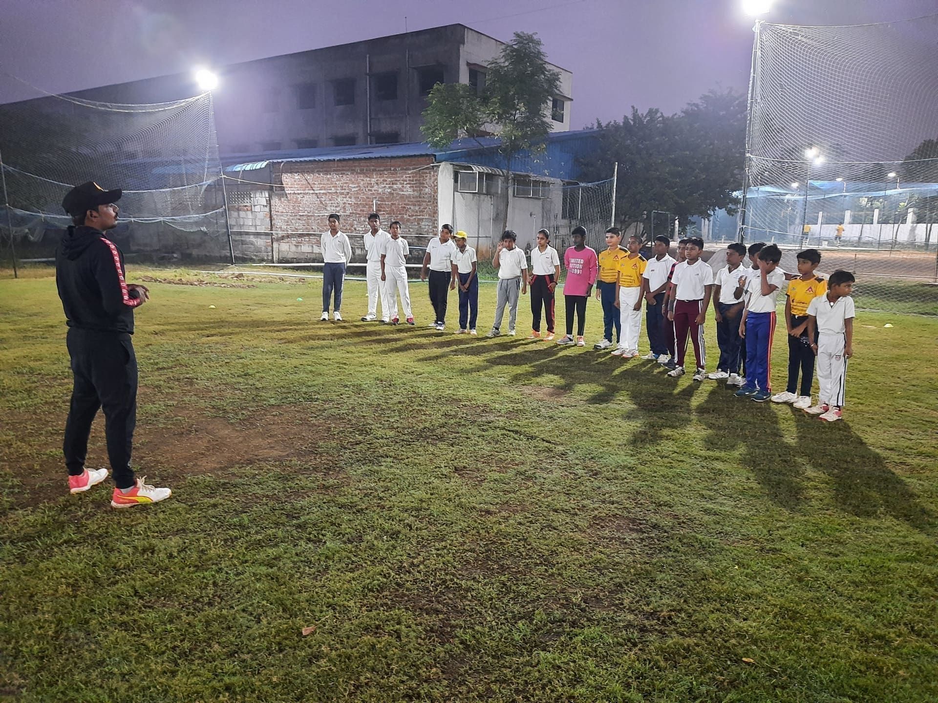 Coach addressing a line of junior cricketers under floodlights
