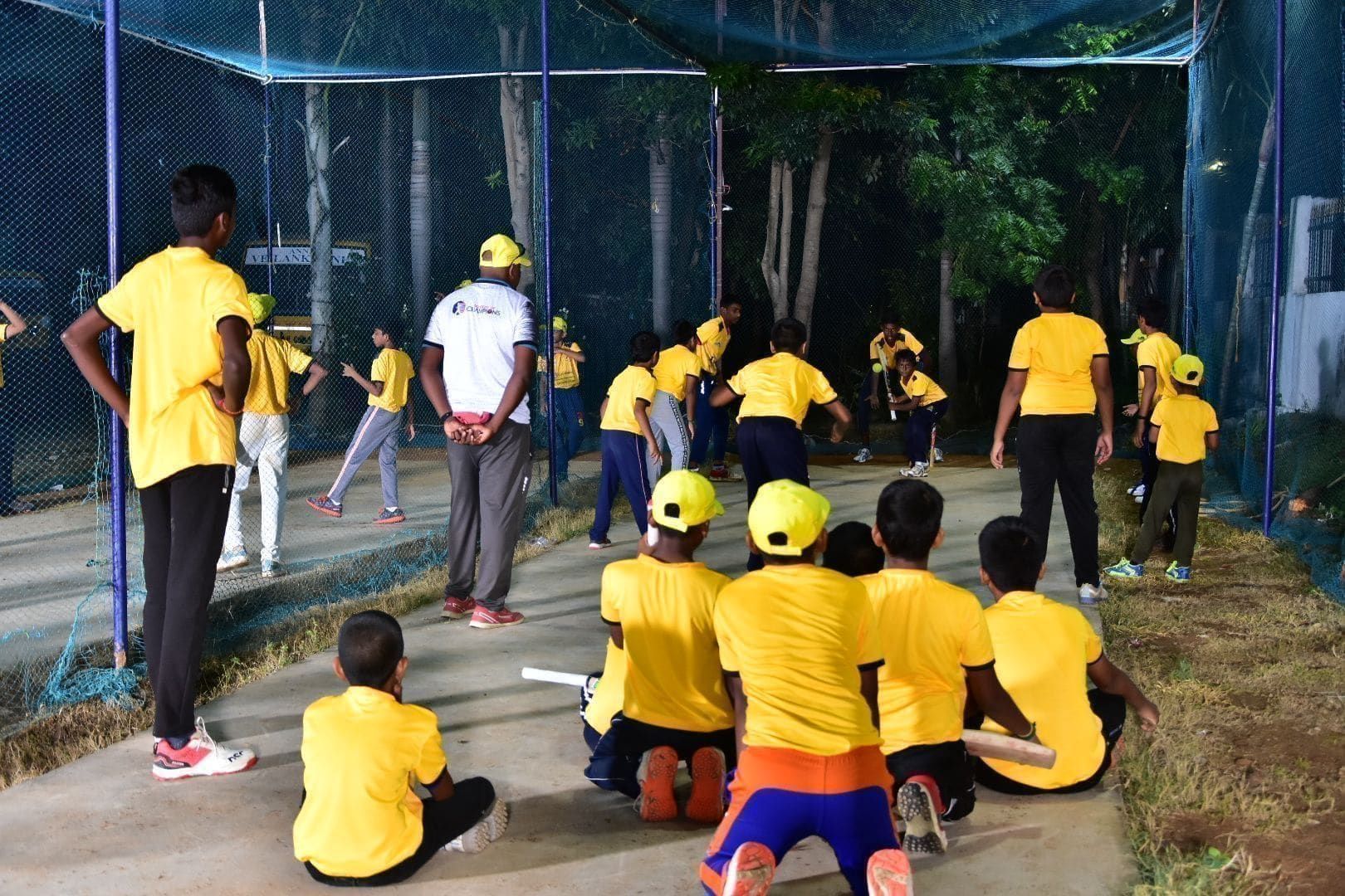 Young players watching a coaching demonstration inside cricket nets