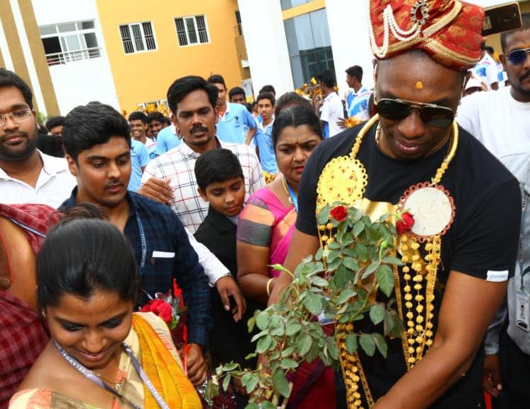 Cricket guest wearing a ceremonial crown and garlands among students