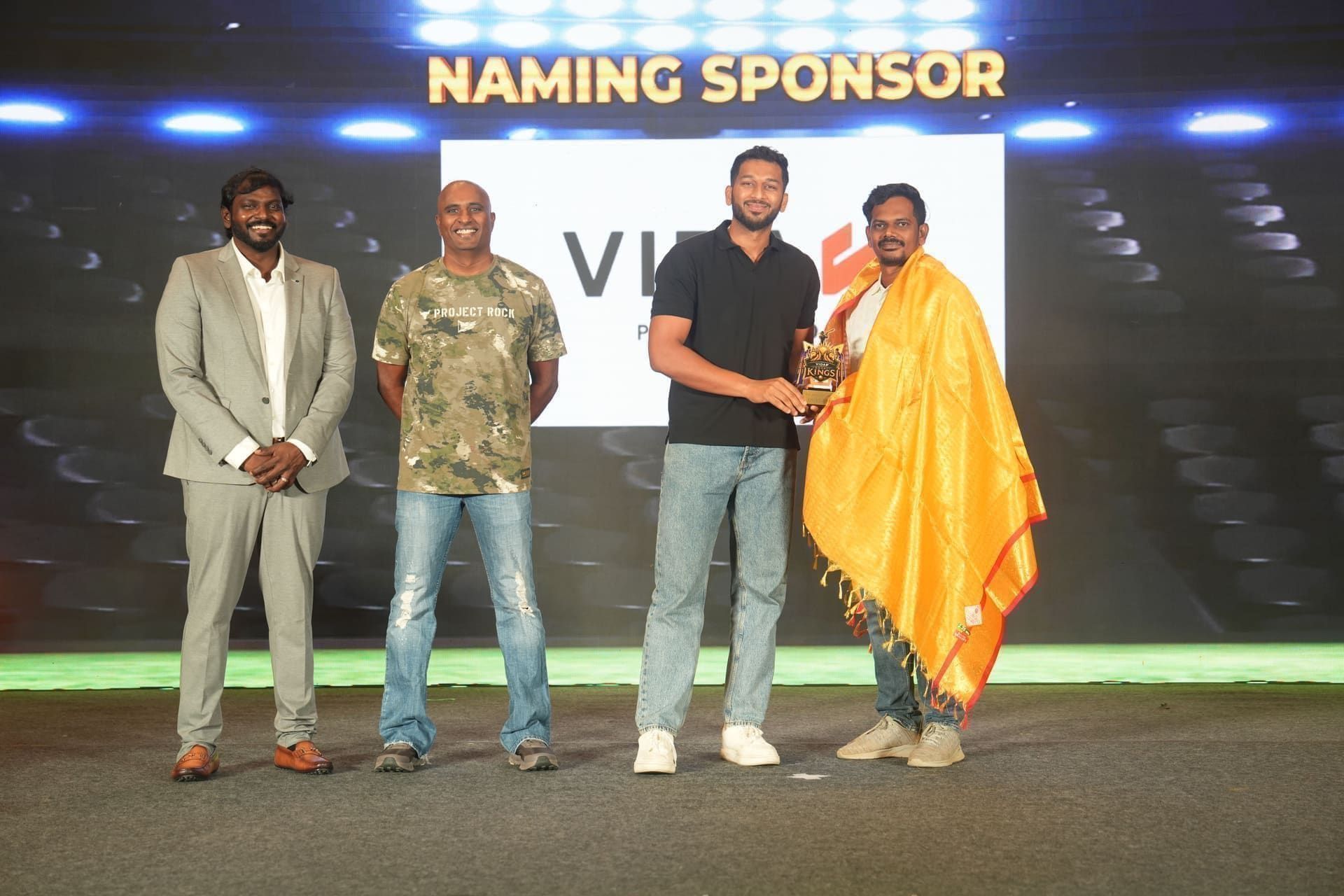 Trophy presentation on stage under a Naming Sponsor banner