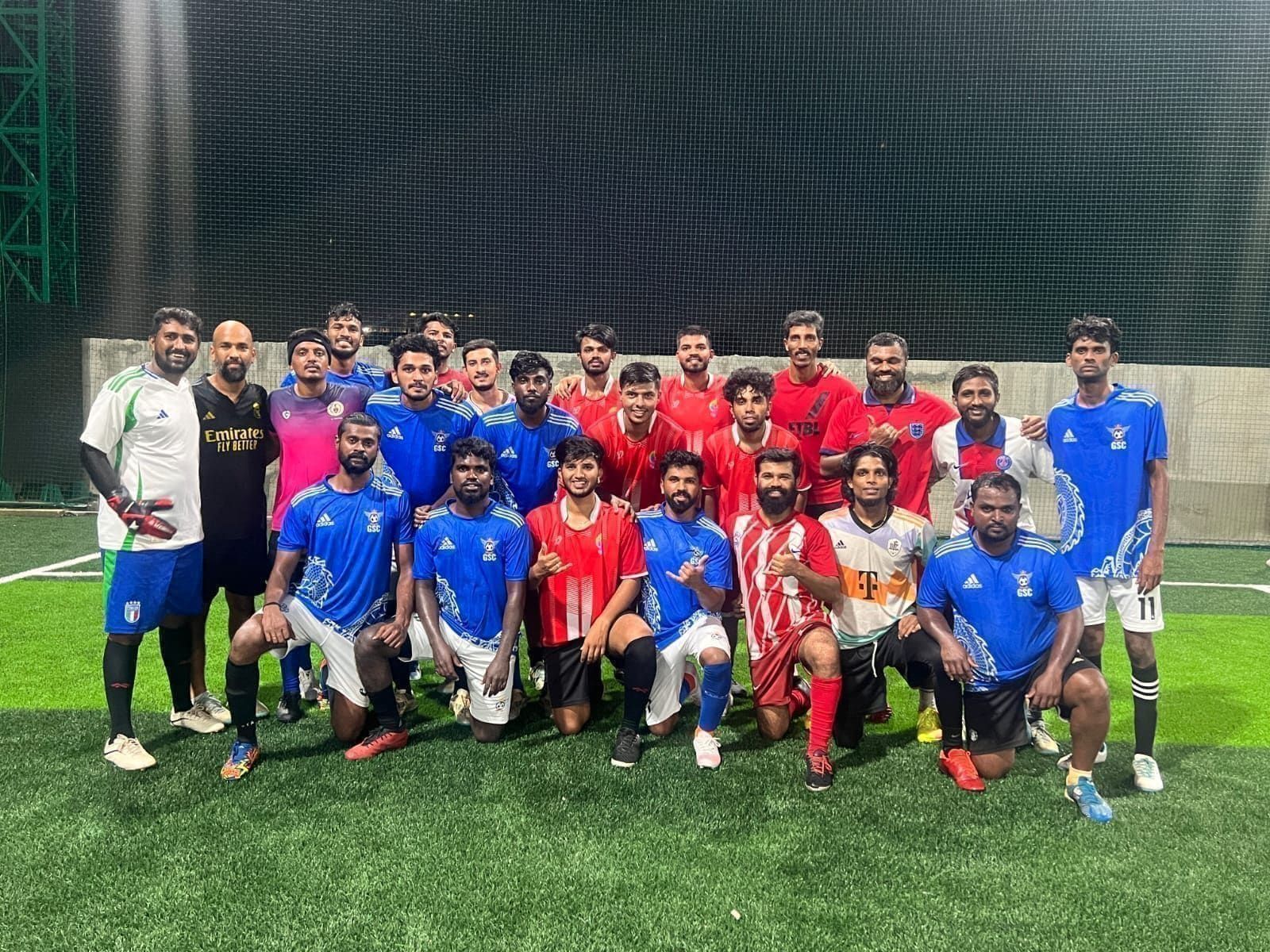 Players posing together on a floodlit football pitch