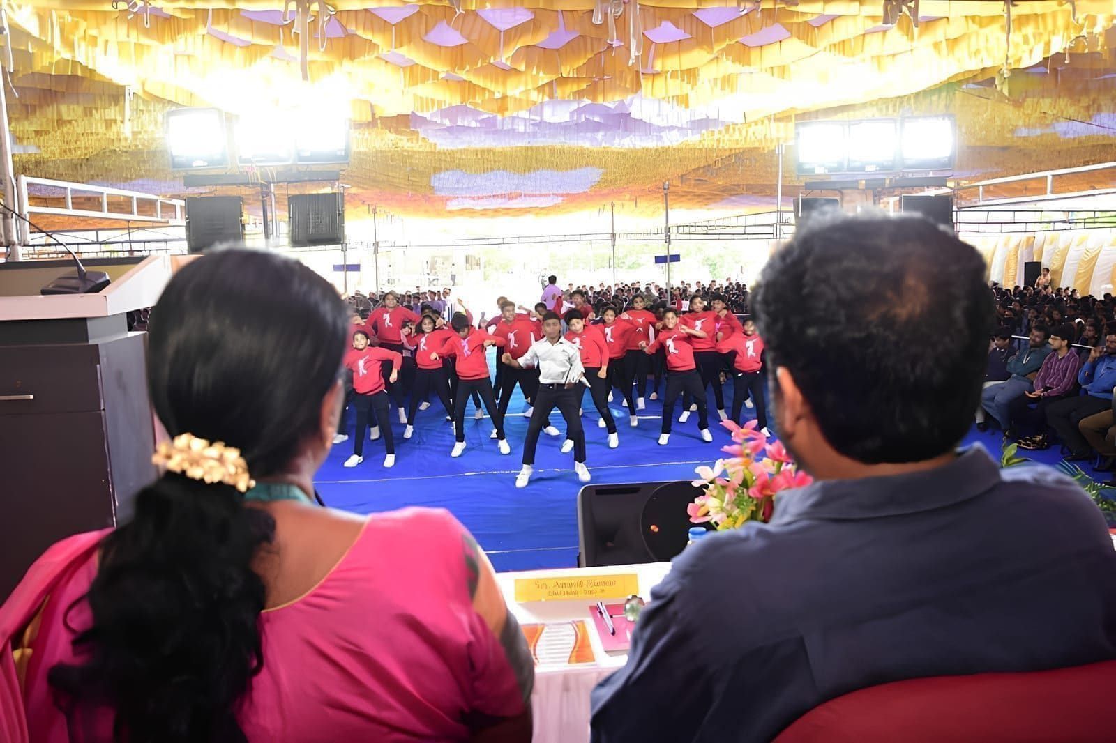 Students performing in front of seated guests under a decorated canopy