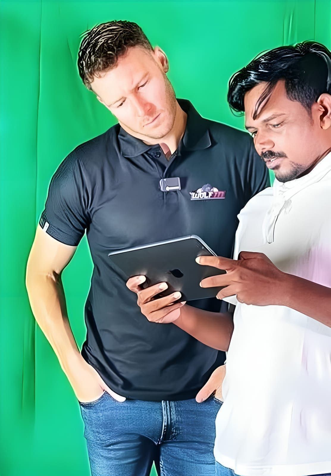 Two people reviewing a tablet in front of a green screen